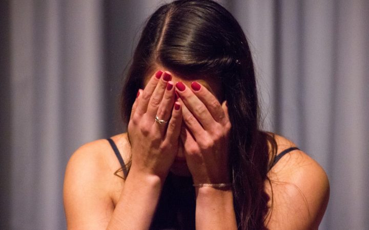 woman in black tank top covering her face with her hands