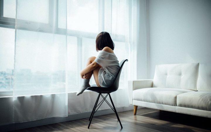 woman sitting on black chair in front of glass-panel window with white curtains